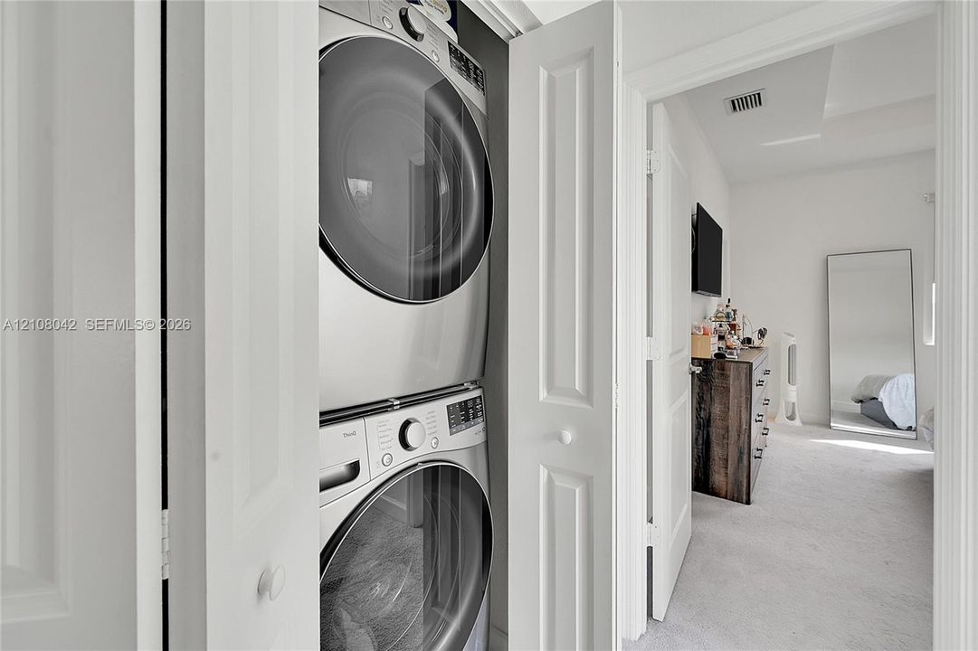 Laundry closet featuring a stacked front-loading washer and dryer set with metallic finish and bifold doors