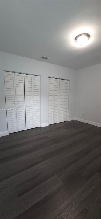 Room featuring wood-finish flooring, two sets of white louvered-door closets, and a central flush-mount ceiling light fixture