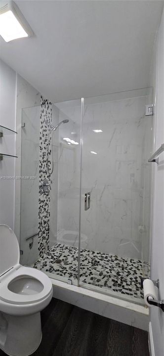 Walk-in shower featuring a frameless glass door, stone-finish mosaic floor tile, accent tile wall detail, and chrome shower fixtures