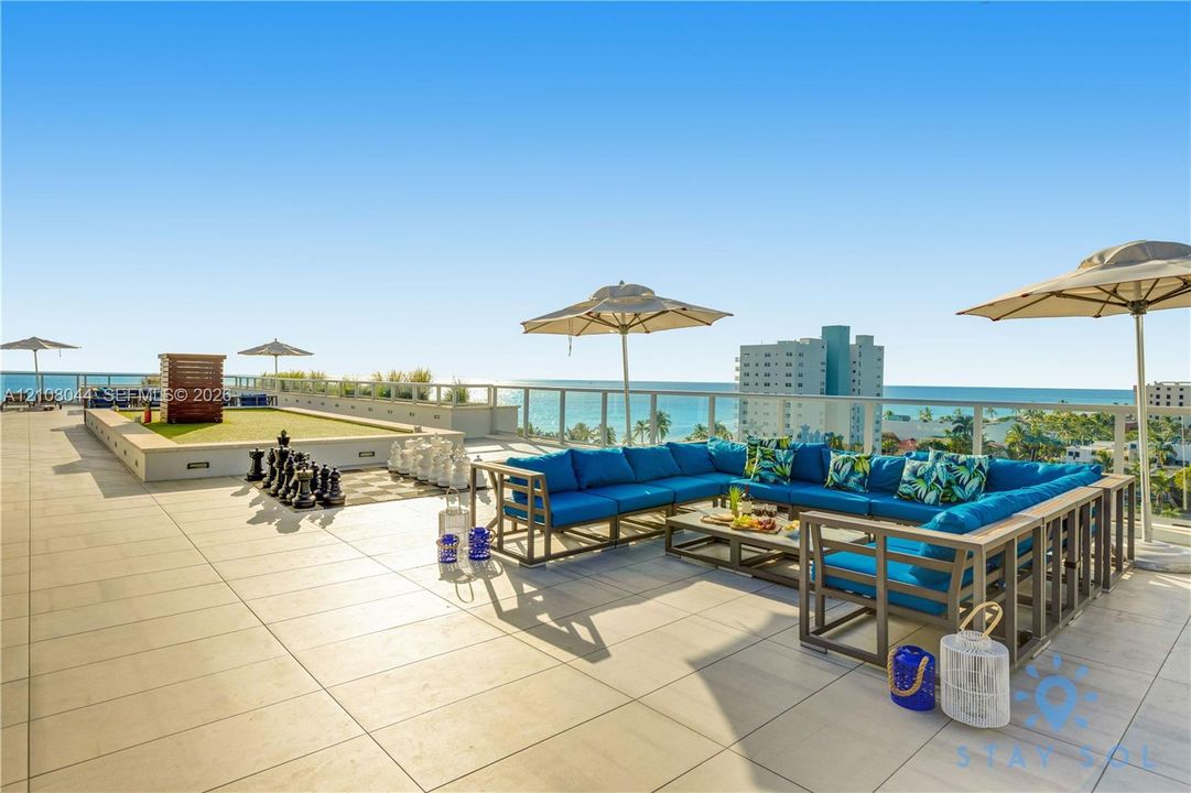 Expansive rooftop terrace featuring large-format tile flooring, a glass-panel railing system, and an integrated turf recreation area
