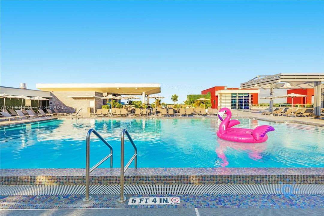 Swimming pool with a tile-trimmed edge, stainless steel ladder, and surrounding paved deck with covered structures