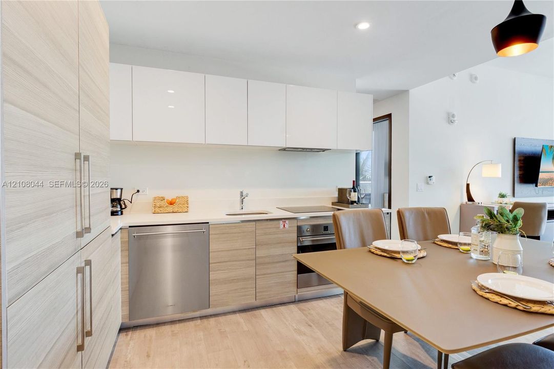 Modern kitchen featuring high-gloss white upper cabinetry, wood-finish lower cabinetry, integrated stainless steel dishwasher, built-in cooktop, and recessed lighting
