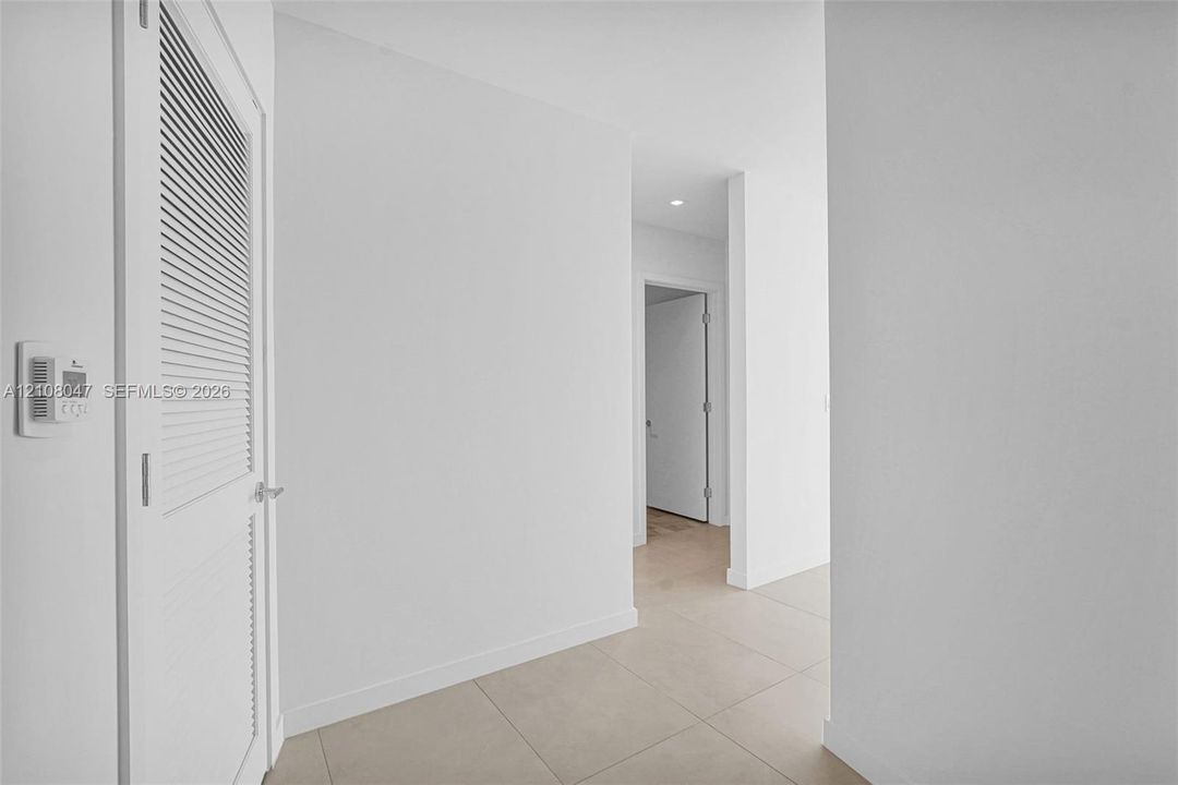 Louvered door, neutral tile flooring, recessed lighting, and crisp white walls