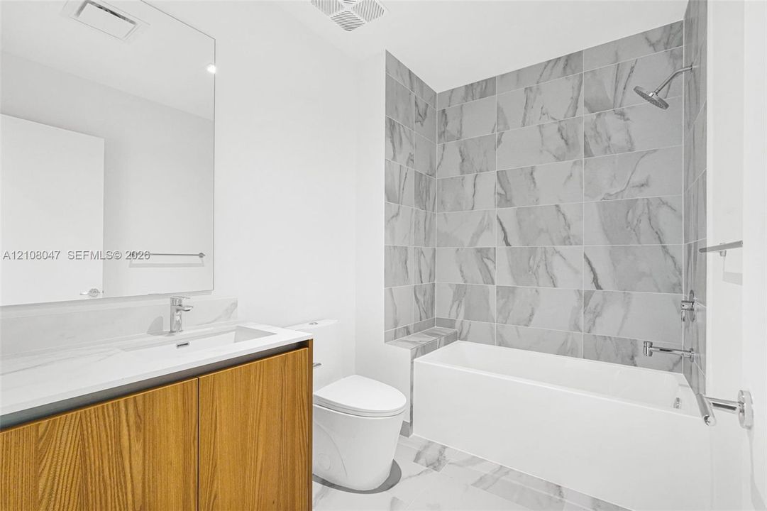 Bathroom featuring a floating wood-finish vanity, integrated sink, large format tile flooring, and a tiled shower with an integrated bench