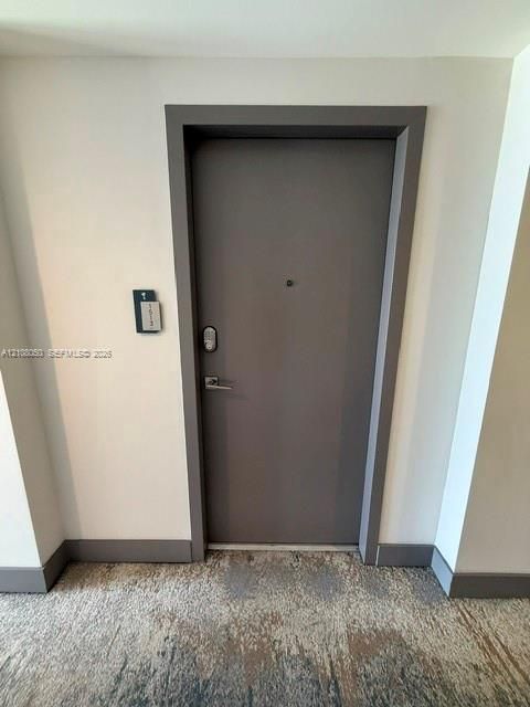 Solid core entry door featuring a matte finish, electronic keypad lock, and integrated peephole, framed by a charcoal-toned door casing and matching trim