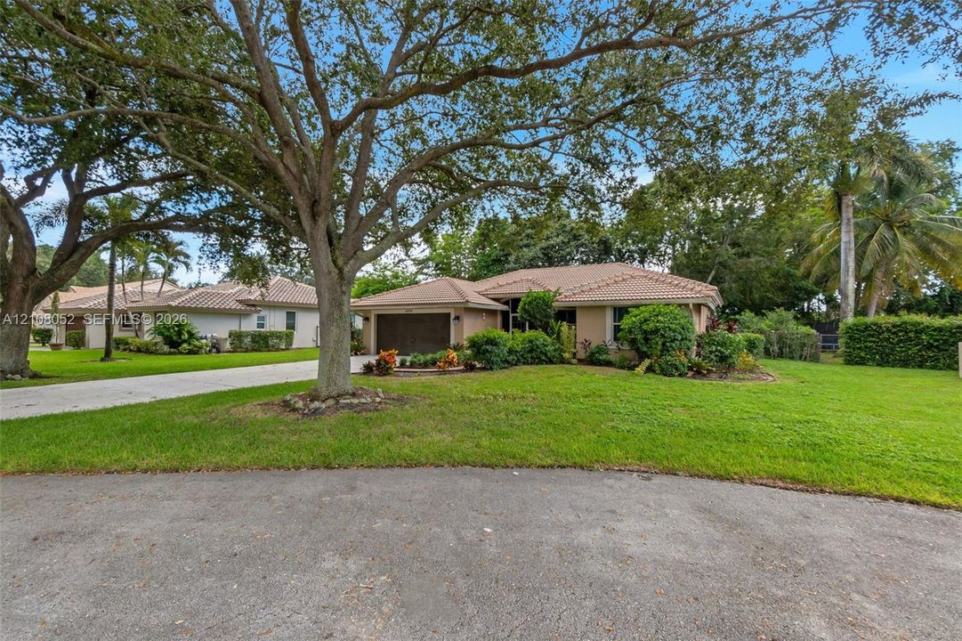 Single-story residence featuring a tiled roof, stucco exterior, attached garage, concrete driveway, and mature landscaping