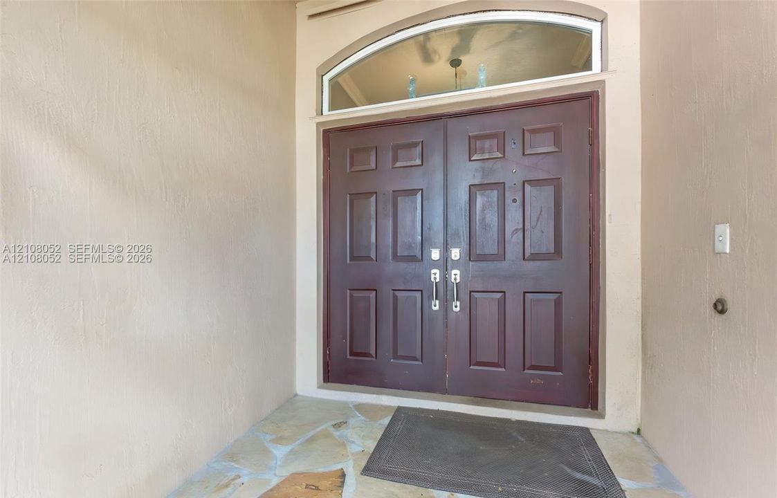 Double-door entryway featuring a dark wood-finish, six-panel design with a semicircular transom window and natural stone flooring