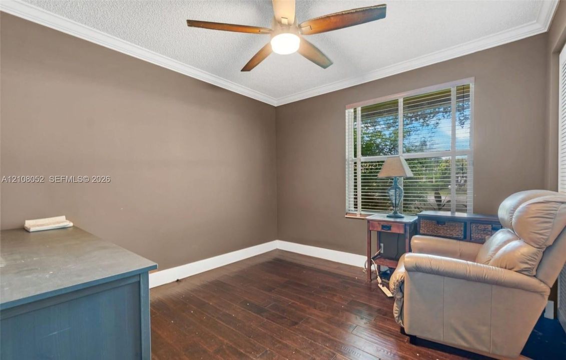 Room featuring dark-toned wood-finish flooring, crown molding, and a central ceiling fan with an integrated light fixture