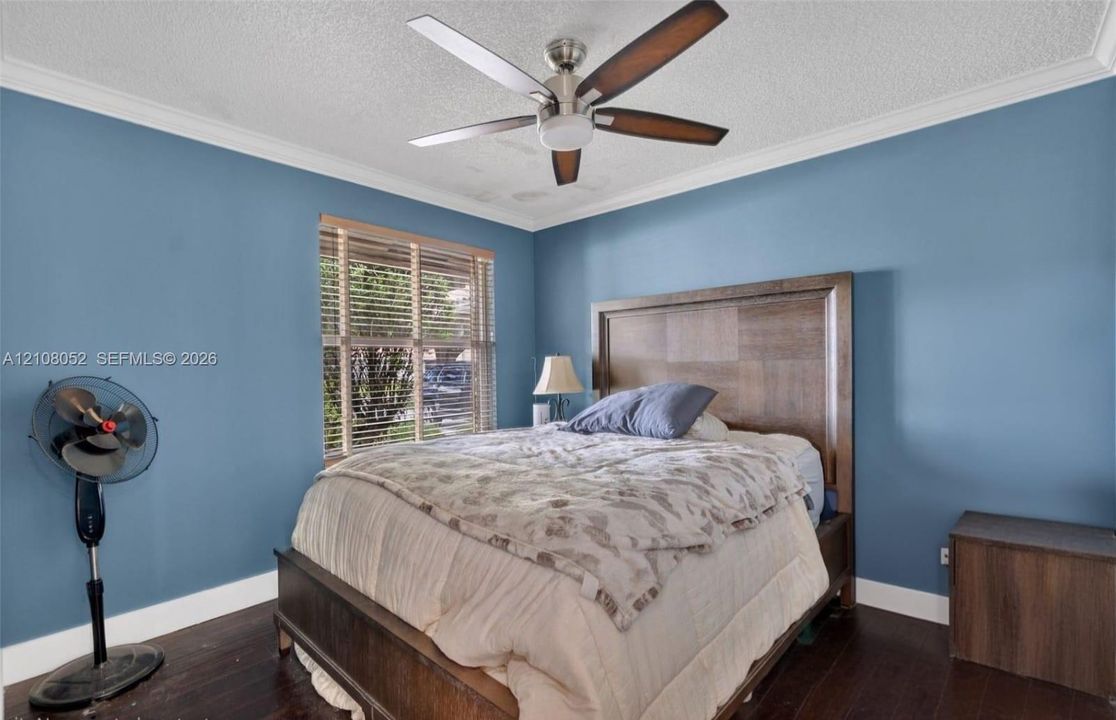 Room featuring dark wood-finish flooring, crown molding, a central ceiling fan with integrated light fixture, and horizontal window blinds