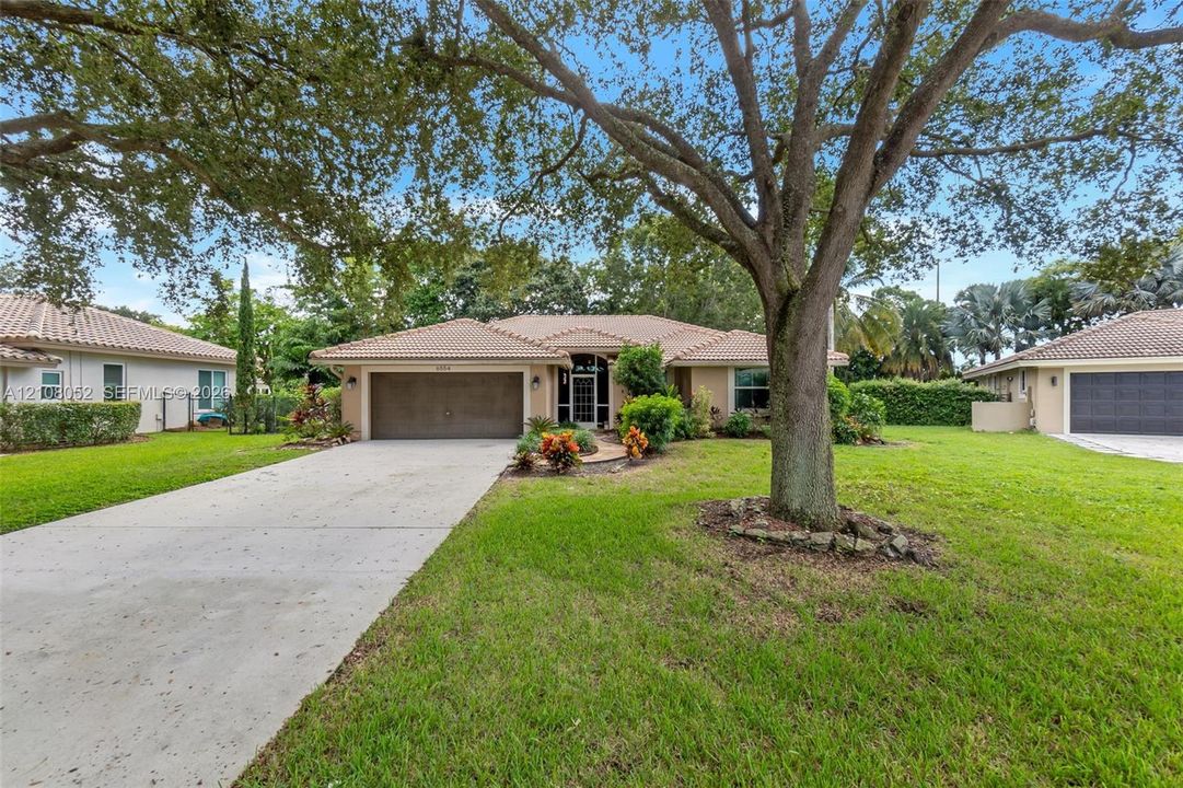 Single-story residence featuring a tile roof, stucco exterior, concrete driveway, two-car garage, and mature landscaping