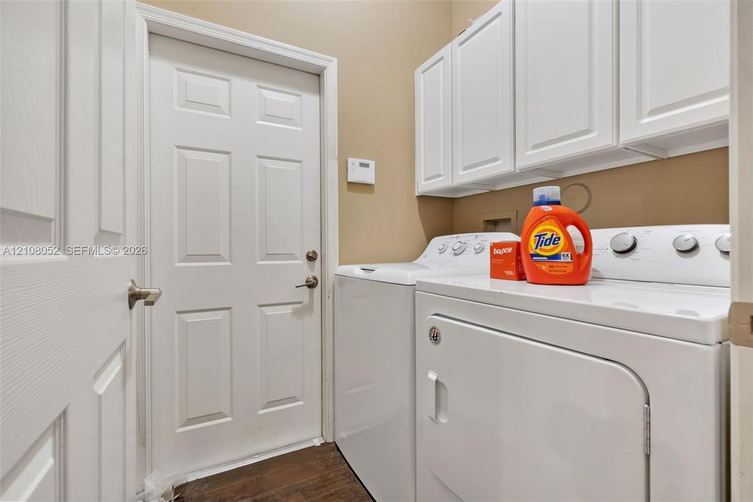 Utility space featuring white shaker-style cabinetry, wood-finish flooring, and a six-panel interior door