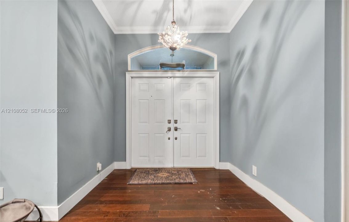 Entryway featuring double doors with a semi-circular transom window, wood-finish flooring, crown molding, and a tiered crystal chandelier