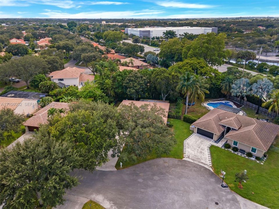 Aerial perspective featuring multi-structure residential property with tile roofing, concrete paver driveways, mature canopy trees, and an outdoor swimming pool