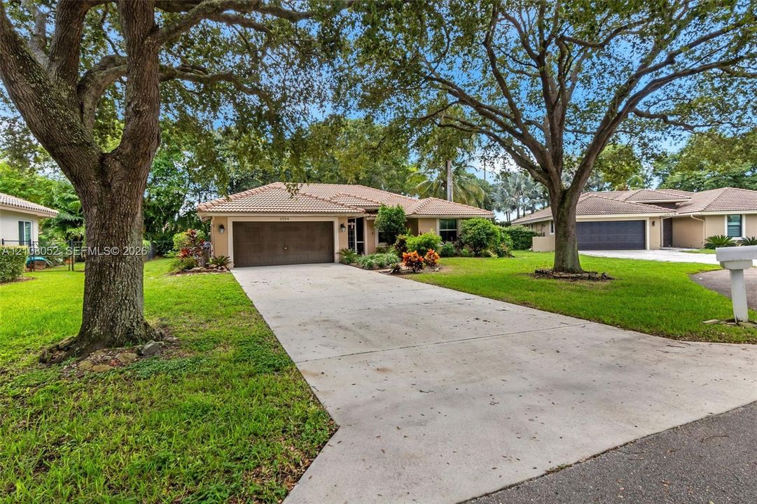 Single-story residence featuring a tile roof, concrete driveway, attached multi-car garage, and mature landscape