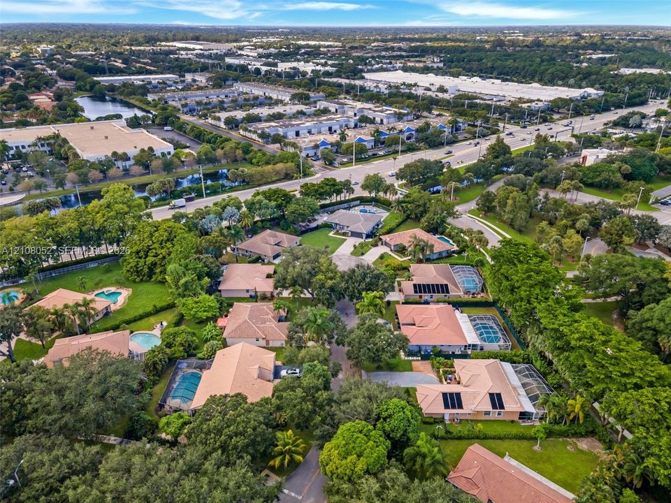 Aerial perspective of a residential neighborhood featuring homes with tile roofs, screened-in swimming pools, mature canopy trees, and manicured lawns