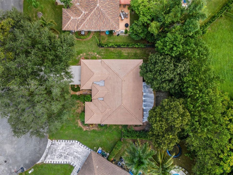 Aerial perspective of a residence featuring a multi-gable tile roof, paved driveway, mature trees, and landscaped grounds
