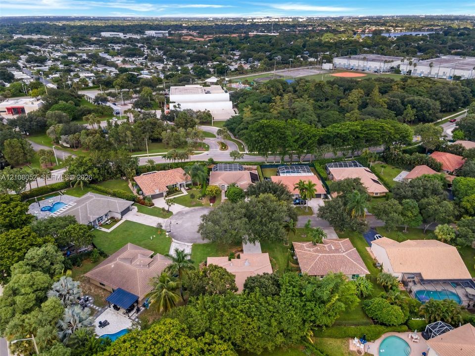 Aerial perspective of a suburban neighborhood featuring low-density residential zoning, mature tree canopy coverage, cul-de-sac street infrastructure, and multiple properties with integrated swimming pools