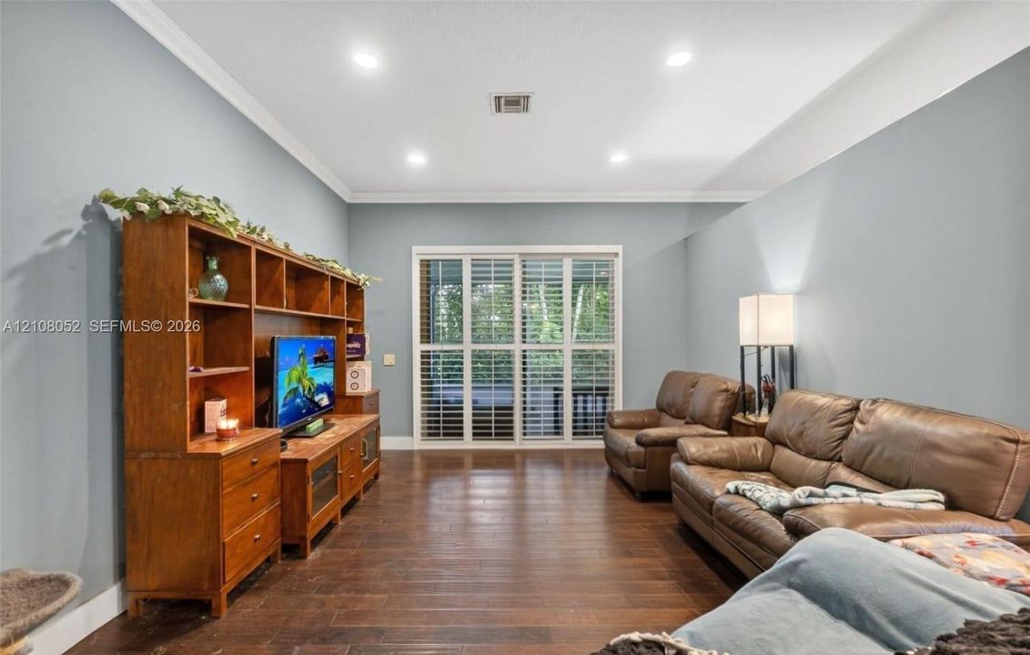 Living area featuring dark-tone wood-finish flooring, recessed lighting, crown molding, and glass sliding doors with shutter accents