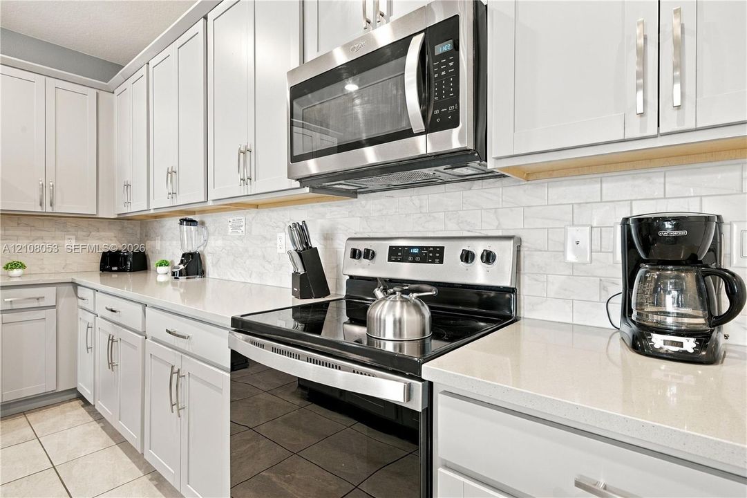 Kitchen featuring light gray shaker-style cabinetry, quartz countertops, subway tile backsplash, stainless steel microwave, and slide-in range