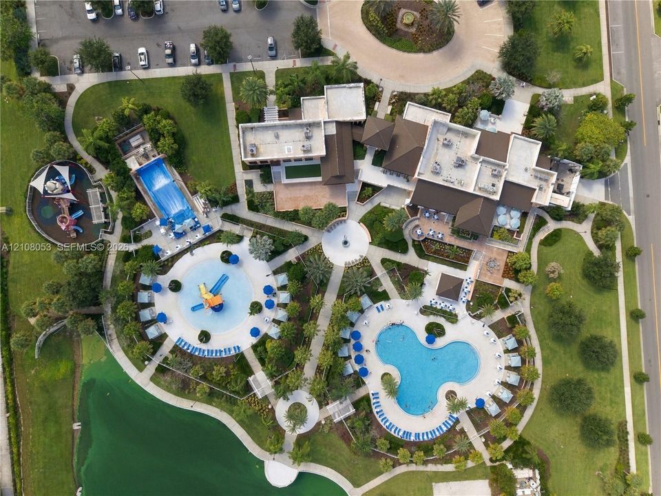 Aerial perspective of community facilities featuring multiple outdoor swimming pools, a water play area with slides, paved walkways, and landscaped grounds