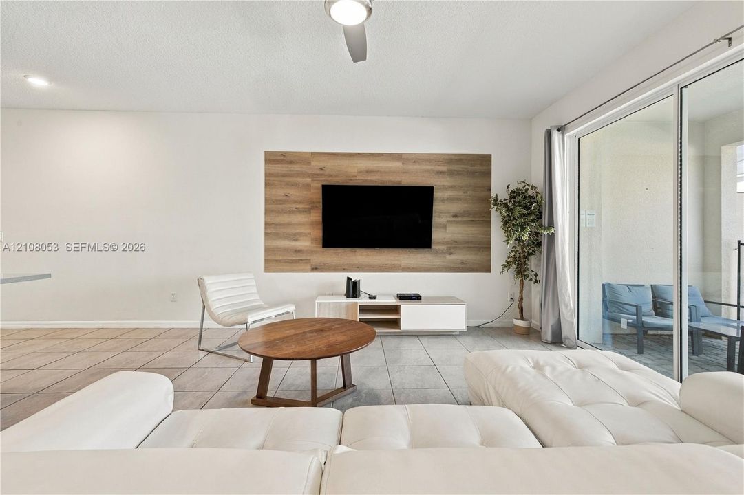 Living area featuring large-format tile flooring, a wood-finish accent wall, ceiling fan, and sliding glass doors