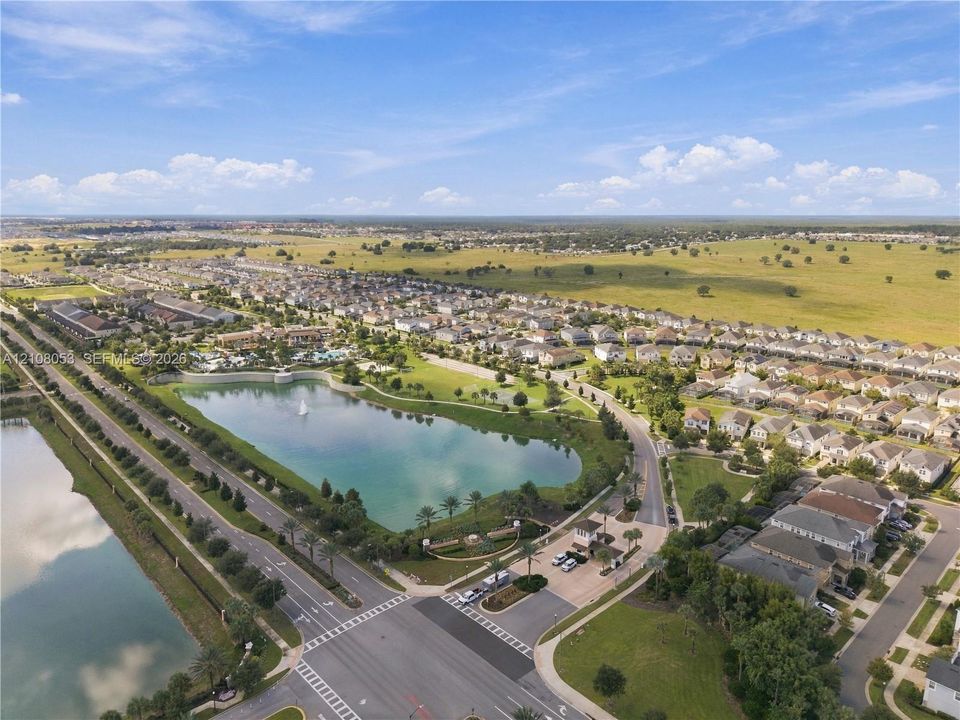 Aerial perspective of a master-planned community featuring a central lake with fountain, gated entry, paved roadways, and landscaped green space