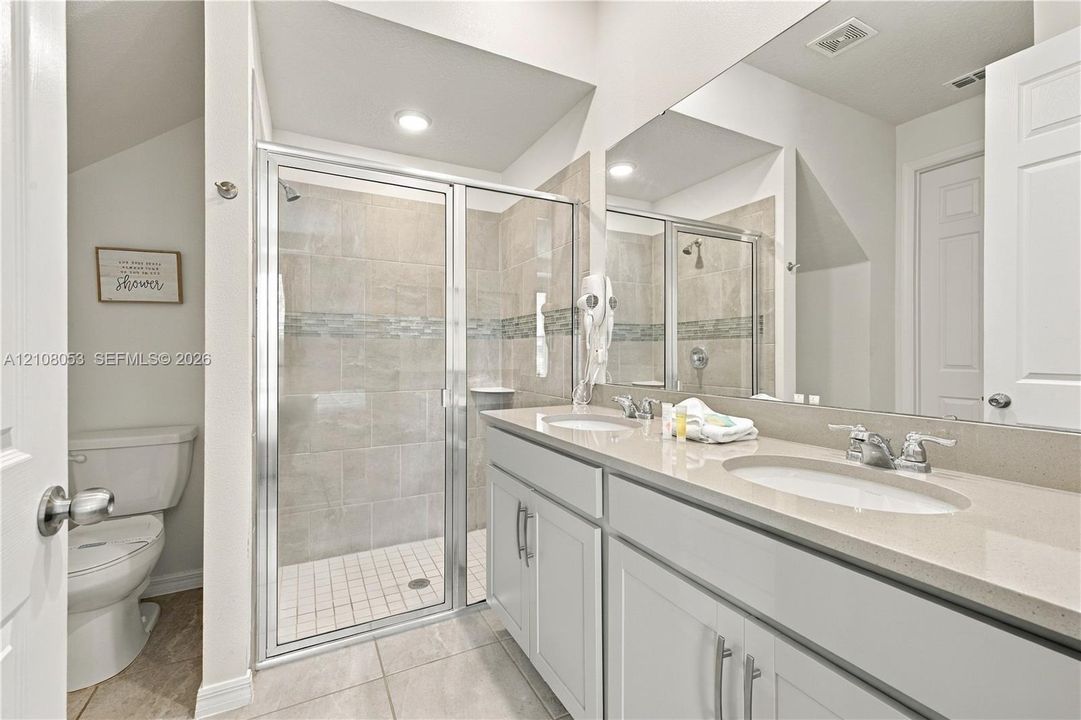 Dual vanity with a stone-surface countertop, full-width mirror, glass-enclosed shower with tiled surround, and ceramic tile flooring