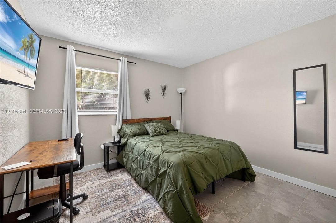 Neutral-toned interior space featuring light-colored wall paint, large-format tile flooring, and a single window with a black curtain rod