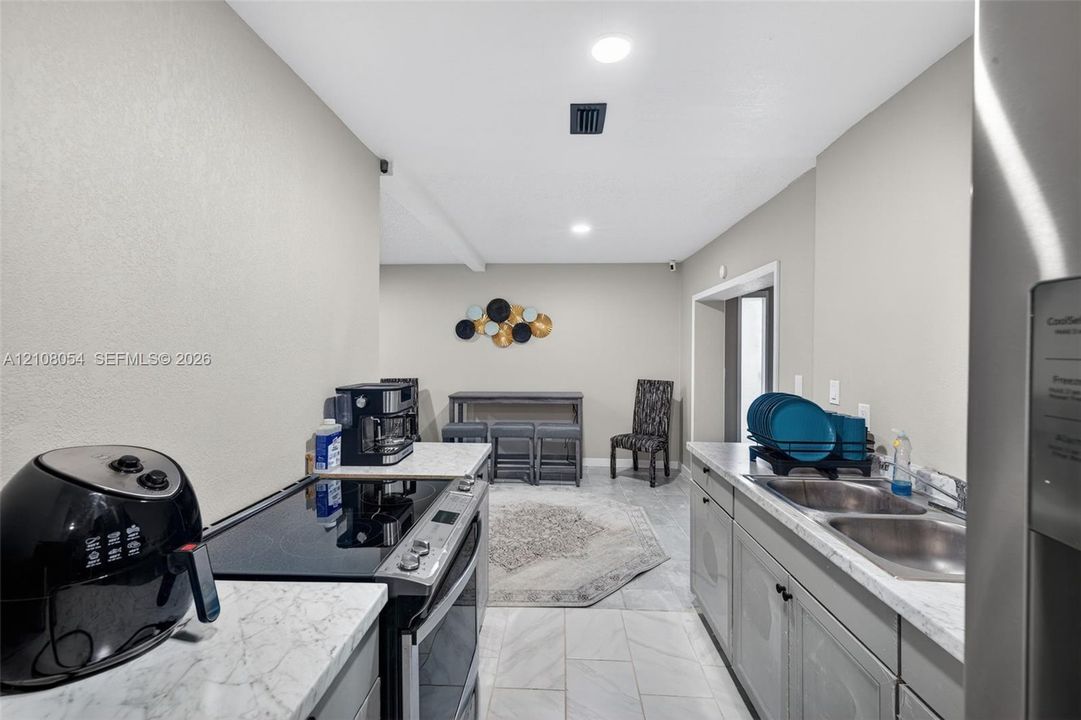 Kitchen featuring light-gray cabinetry, stone-finish countertops, stainless steel dual-basin sink, electric range, and light-tone tile flooring