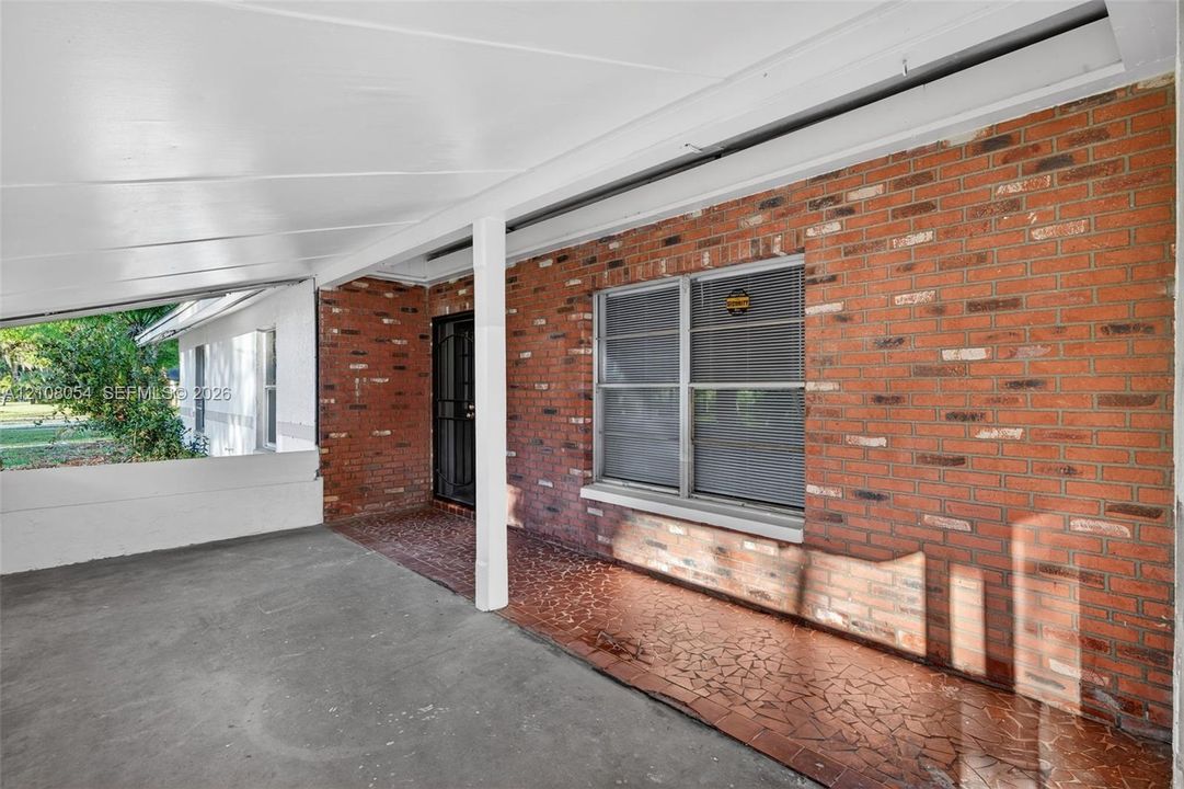 Covered porch featuring a red brick facade, concrete flooring, mosaic tile accent inlay, and metal window screens