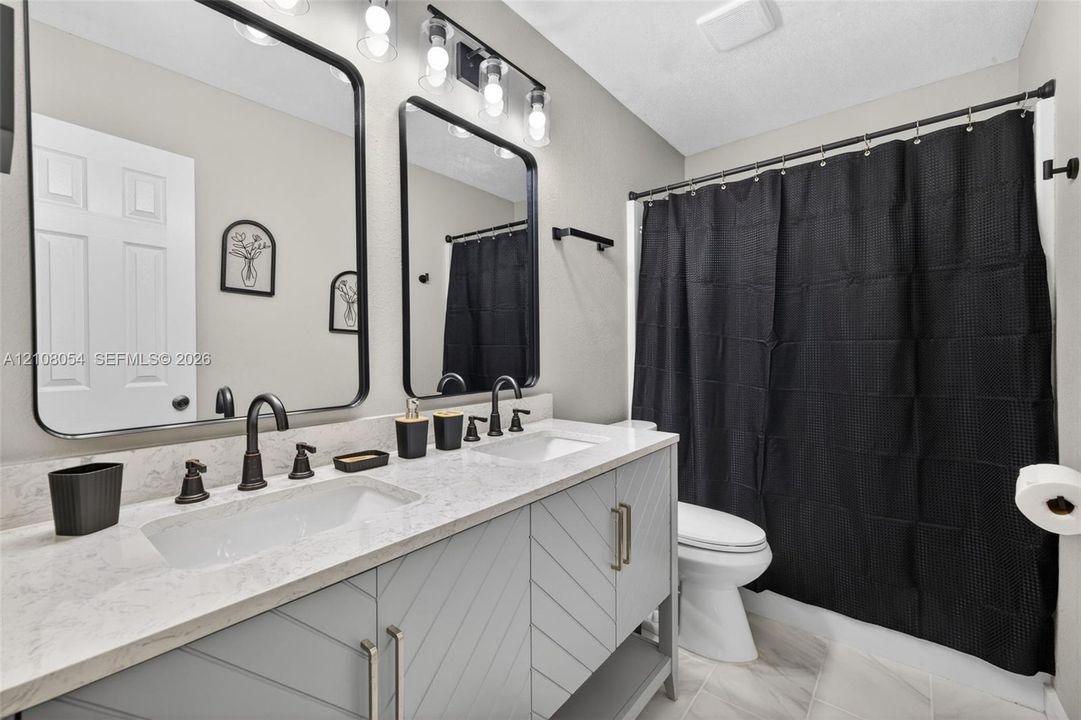 Dual-sink vanity featuring a light-toned stone countertop, chevron-patterned cabinetry, arched black-framed mirrors, and matte black plumbing fixtures