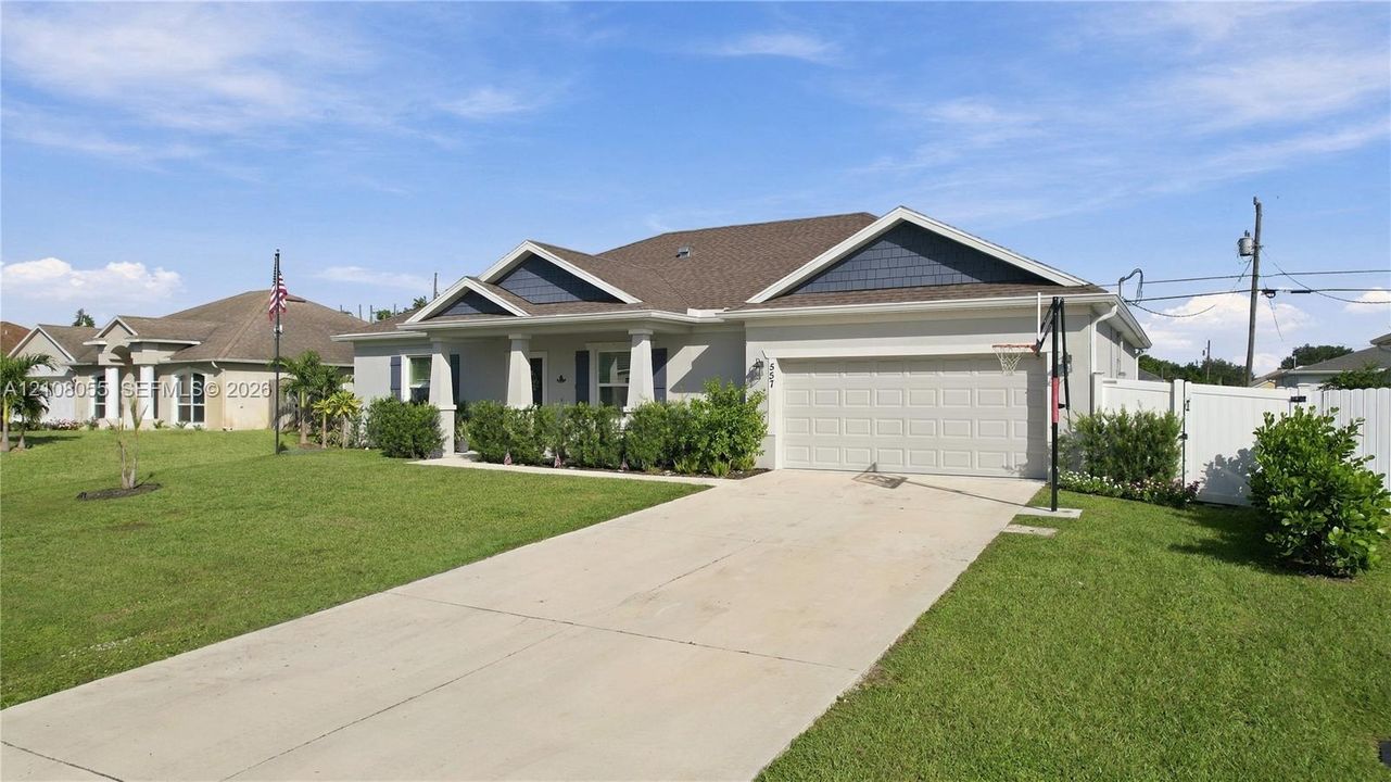 Single-story residence featuring a multi-gable roofline, a two-car garage, a covered front porch with decorative columns, and white vinyl privacy fencing