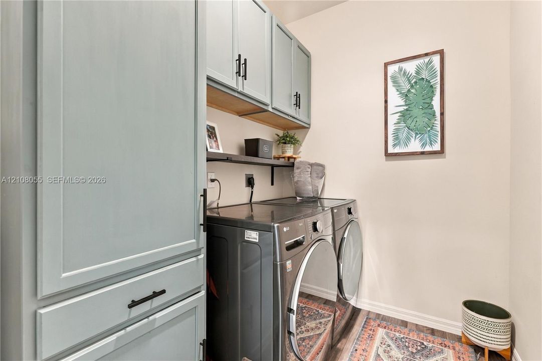 Utility area featuring custom-painted cabinetry with matte black hardware, integrated open shelving, and wood-finish flooring