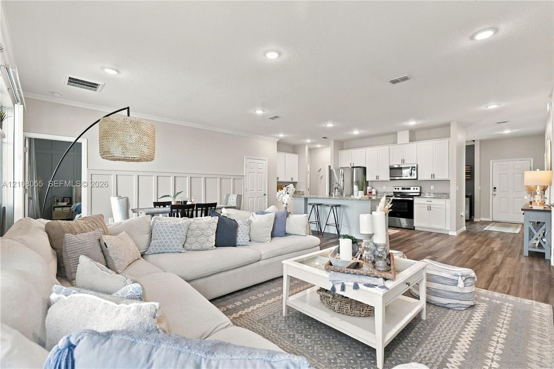 Open-concept floor plan featuring wood-finish flooring, recessed lighting, white cabinetry, a kitchen island, and wainscoting detail