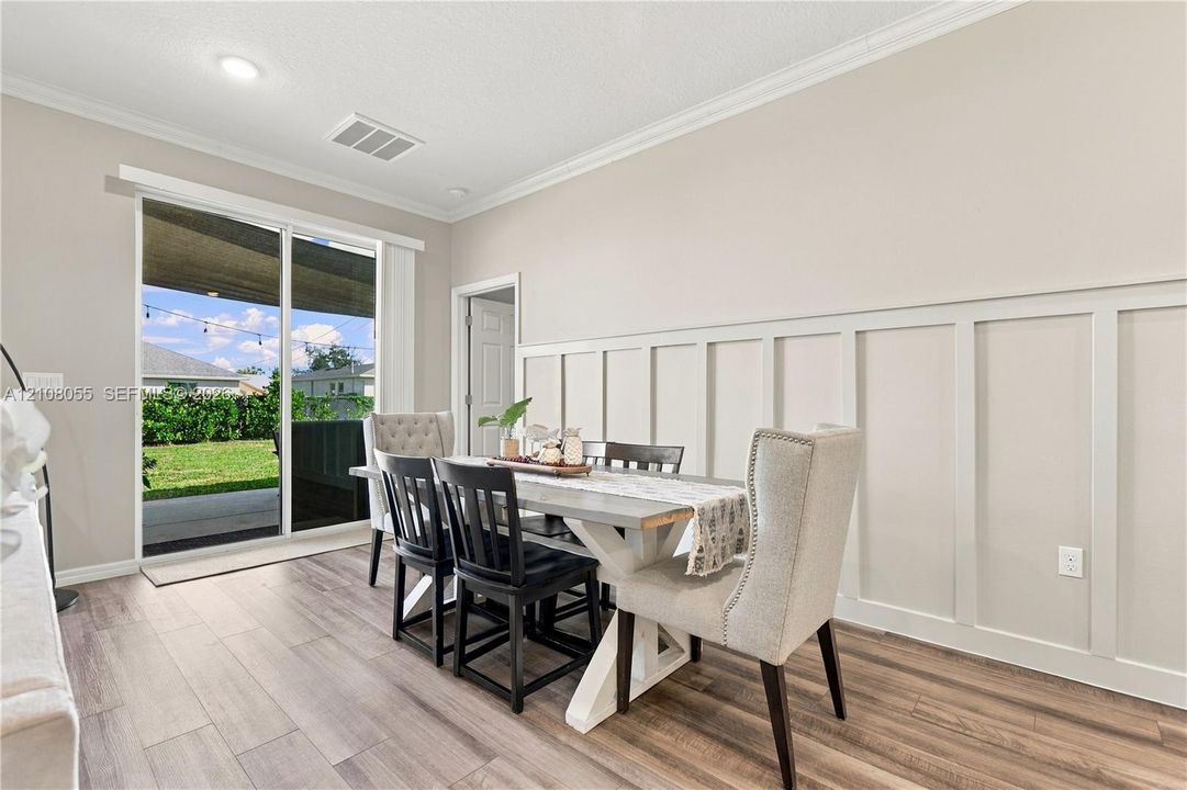 Neutral-toned room featuring wood-finish flooring, white board-and-batten wainscoting, crown molding, and a sliding glass door providing external access