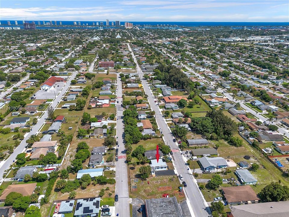 Aerial perspective of a corner lot property featuring an asphalt-shingled roof and exterior hardscaping, situated in proximity to coastal waterfront and urban infrastructure