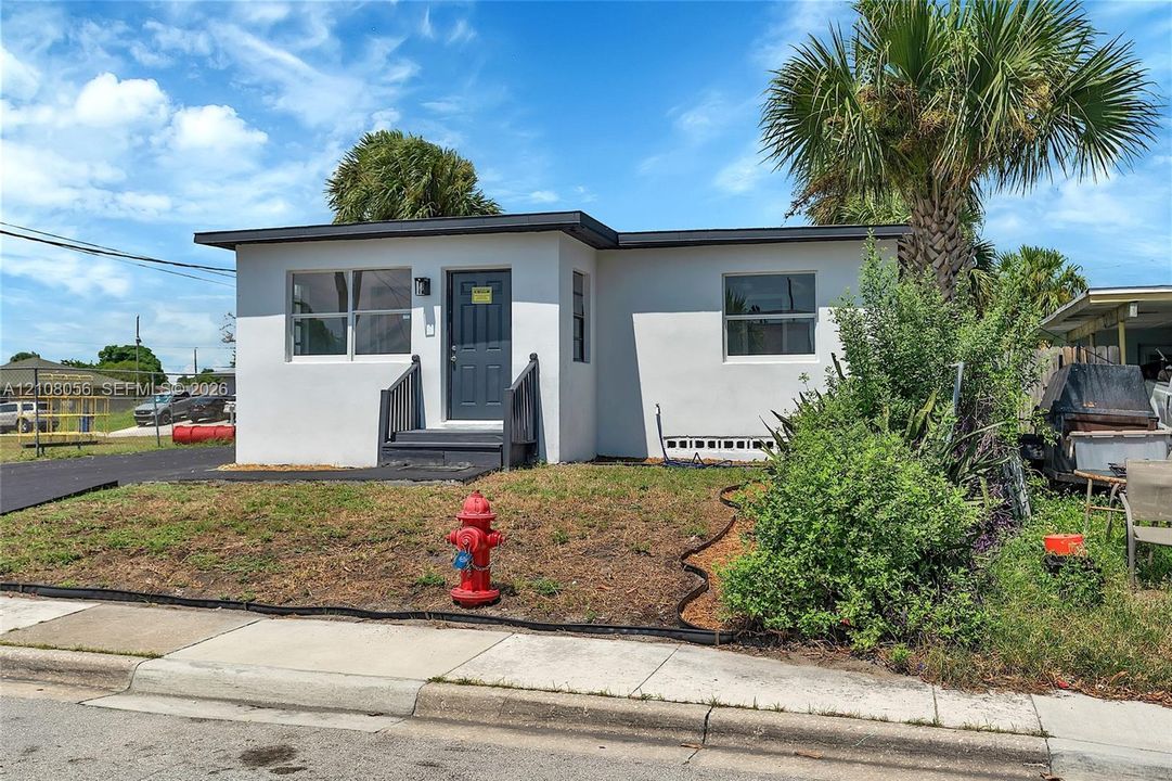 Single-story exterior featuring a white stucco facade, flat roofline, dark-toned entry door, and paved driveway