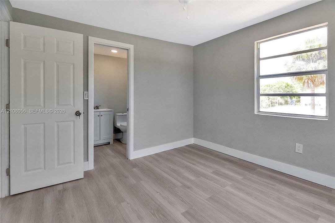 Room featuring neutral-toned walls, wood-finish flooring, a multi-pane window, and a six-panel door leading to a bathroom with a vanity cabinet and toilet