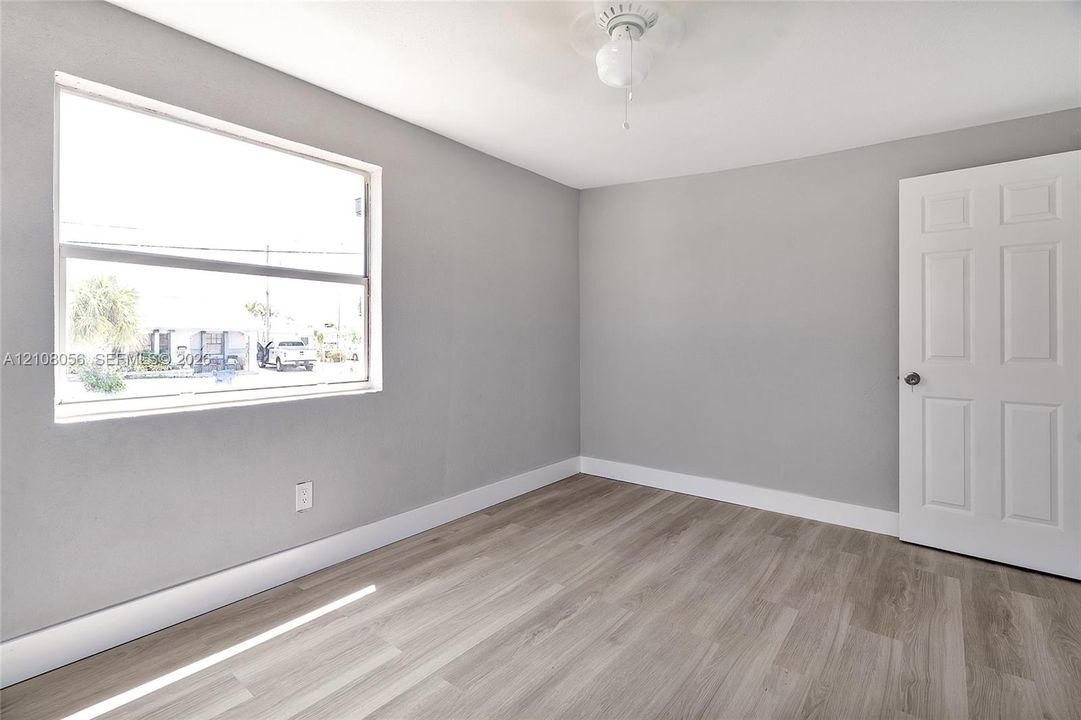 Neutral-toned interior featuring wood-finish flooring, a large single-pane window, and a six-panel door with brushed metal hardware