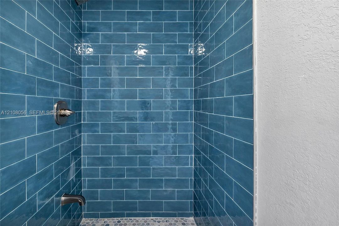 Shower enclosure featuring blue subway tile walls, a pebble-finish floor, and metallic hardware