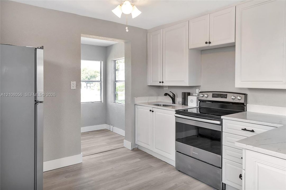 Kitchen featuring white shaker-style cabinetry, stainless steel appliances, light-toned stone-finish countertops, and wood-finish flooring
