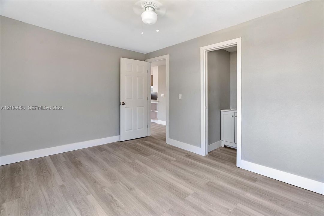 Neutral-toned interior space featuring wood-finish flooring, a ceiling fan with integrated lighting, and a six-panel door