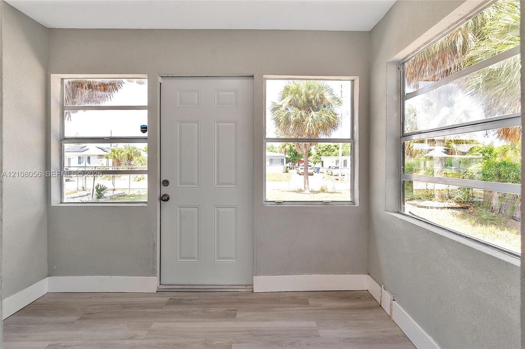 Neutral-toned interior featuring wood-finish flooring, three large windows with horizontal panes, and a six-panel entry door