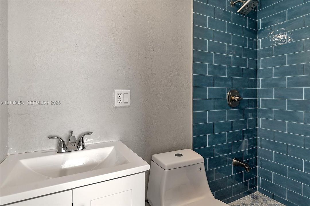 White vanity cabinet with an integrated basin, chrome dual-handle faucet, one-piece toilet, and blue subway-tiled shower surround with chrome fixtures