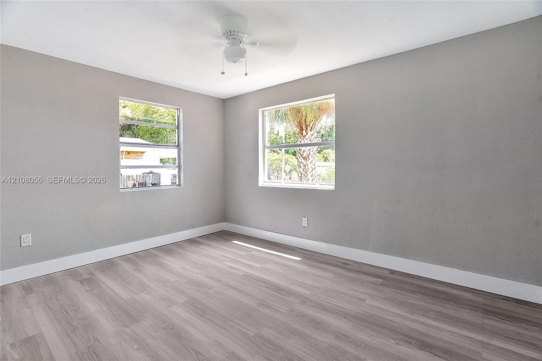 Neutral-toned interior space featuring wood-finish flooring, dual windows, and a ceiling-mounted light fixture with fan