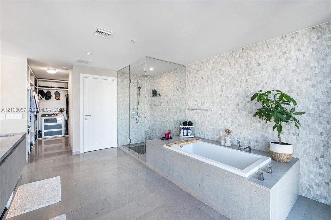 Bathroom featuring a deep-soaking drop-in tub with a stone-surround deck, a seamless glass-enclosed shower, stone mosaic wall tiling, large-format floor tile, and built-in closet shelving