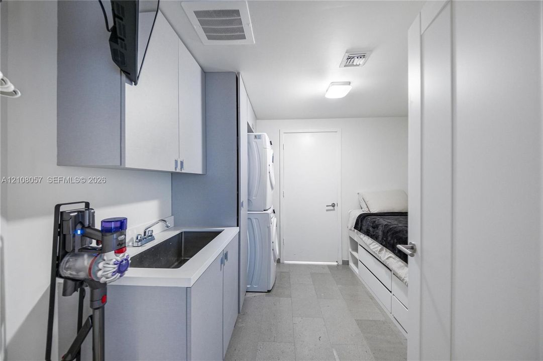 Laundry area featuring built-in cabinetry, an integrated stainless steel basin with a dual-handle faucet, stacked laundry appliances, and tile flooring