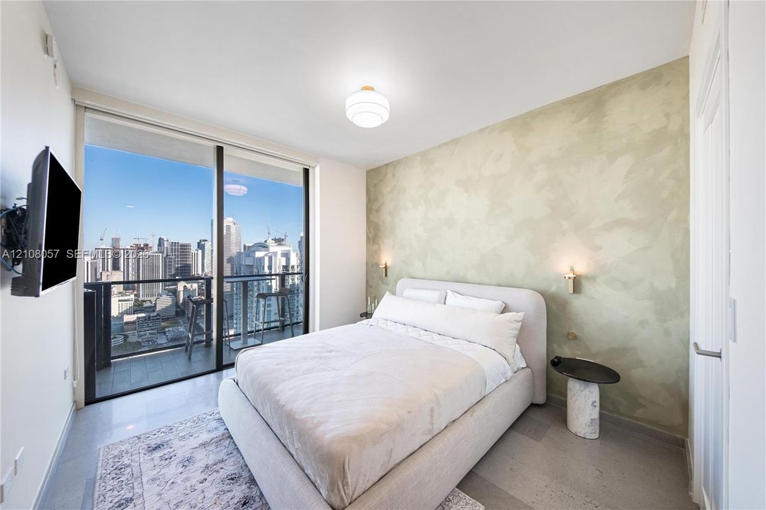Floor-to-ceiling glass sliding doors, private balcony, polished concrete flooring, custom textured wall finish, and wall-mounted brass lighting fixtures