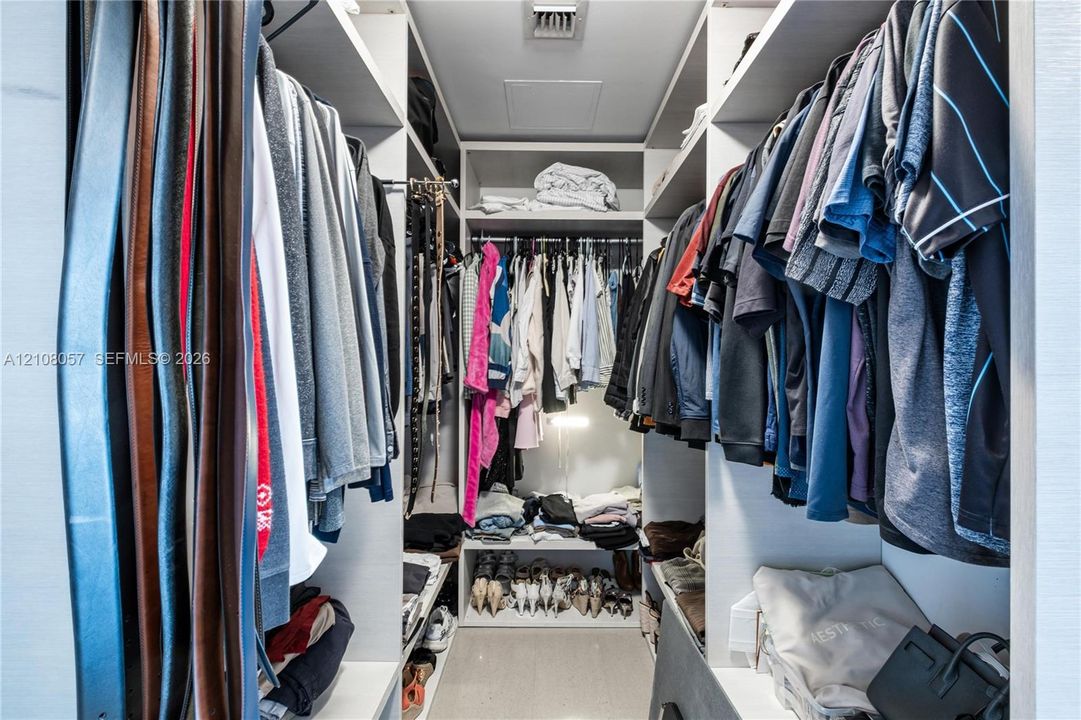 Custom reach-in closet featuring floor-to-ceiling white shelving units, integrated hanging rods, and neutral stone-finish flooring