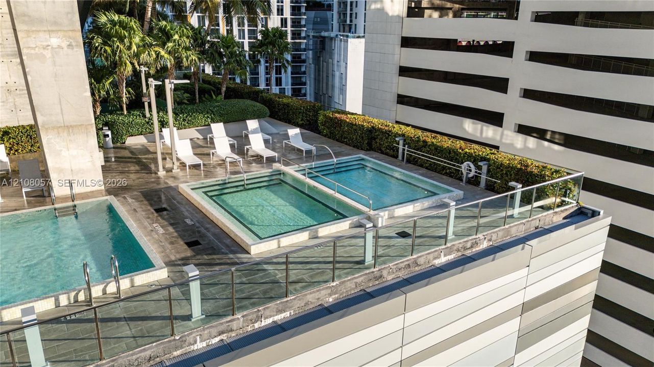 Rooftop terrace featuring multiple swimming pools, tiered hardscaping, manicured hedges, and glass perimeter railings